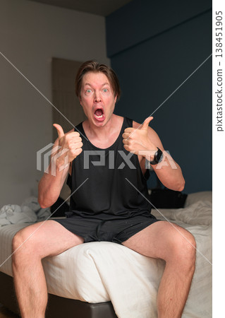 Shocked Caucasian Man Giving Double Thumbs Up on Bed in Minimalist Bedroom Shocked Caucasian Man Giving Double Thumbs Up on Bed in Minimalist Bedroom 138451905