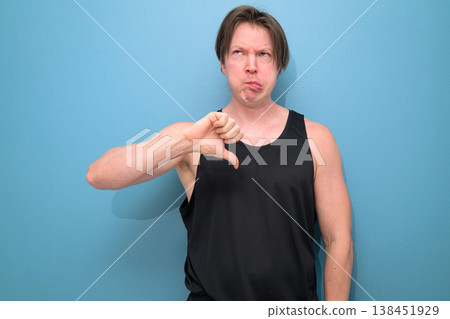 Caucasian Man Giving Thumbs Down and Making Silly Face on Blue Background Caucasian Man Giving Thumbs Down and Making Silly Face on Blue Background 138451929