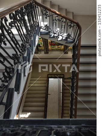 the geometric grace of the staircase within the Tunbridge Wells Town Hall, where the rhythmic descent of stone steps creates a mesmerizing sense of depth. The wrought-iron balustrades, adorned with 138452235