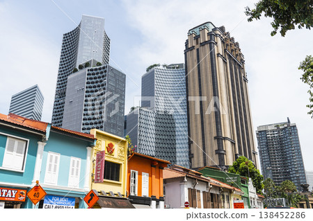 Street view of the traditional shophouses with a skyscraper background in Kampong Glam, Singapore. There are many exotic Middle Eastern restaurants and homeware shops here. Street view of the traditional shophouses with a skyscraper background in Kampong Glam, Singapore. There are many exotic Middle Eastern restaurants and homeware shops here. 138452286