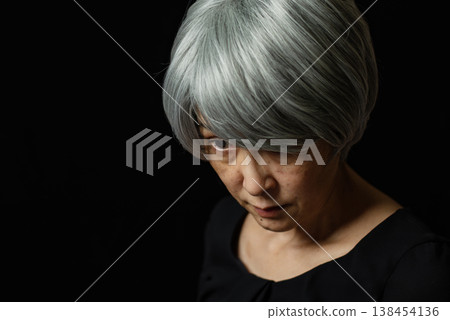 A white-haired senior woman, her eyes lifeless, stares blankly downwards. A white-haired senior woman, her eyes lifeless, stares blankly downwards. 138454136