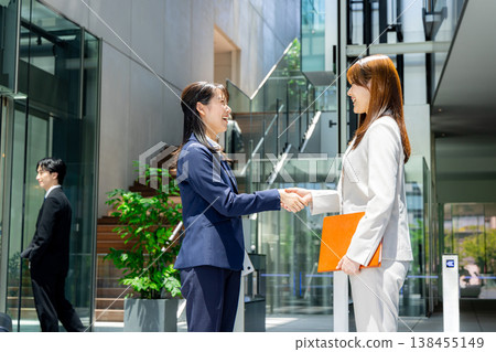 Two businesswomen shake hands in a building. 138455149