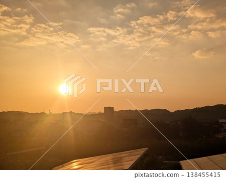 A residential area bathed in the setting sun, with solar panels in the foreground. 138455415