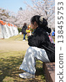 A girl sitting on a bench and looking at the cherry blossoms. 138455753