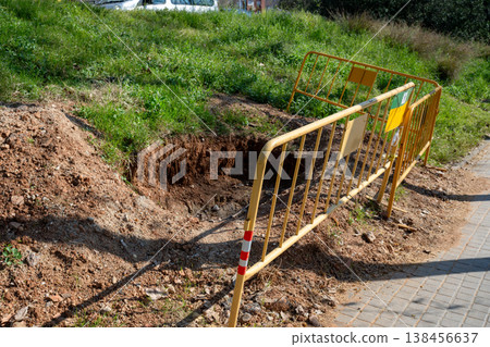Road construction site with excavation hole and safety barrier on sidewalk urban infrastructure maintenance work 138456637