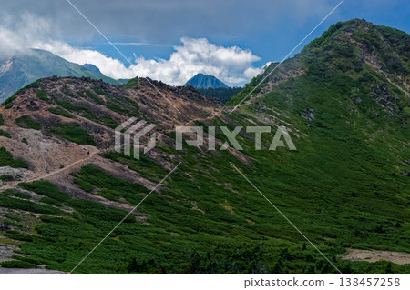 View of Mt. Neishi and the main peaks of the Yatsugatake mountain range shrouded in clouds, seen from the descent of Mt. Higashi-Tengudake. 138457258