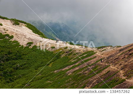 A hiker walking along the ridgeline, surrounded by clouds, as seen from the ascent to Mt. Neishi in the Yatsugatake mountain range. 138457262