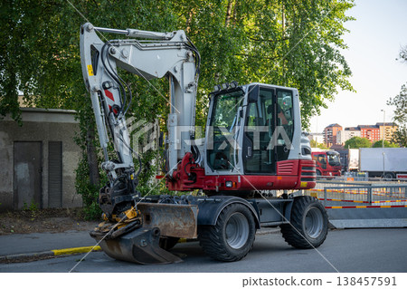 Urban construction excavator parked on street with digging bucket heavy machinery road work infrastructure concept Urban construction excavator parked on street with digging bucket heavy machinery road work infrastructure concept 138457591