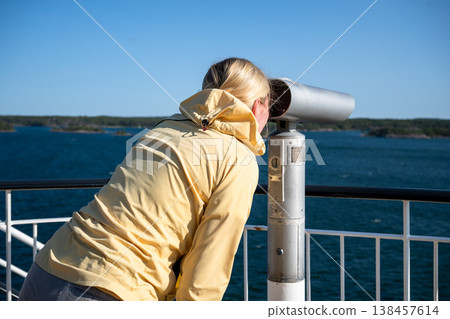 Woman looking through binocular telescope at seaside viewpoint travel tourism exploration coastal landscape concept 138457614