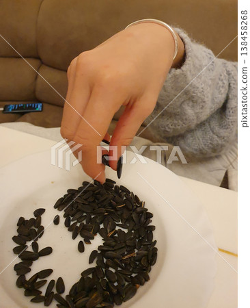 Female hand with manicure takes roasted sunflower seeds from a white plate Female hand with manicure takes roasted sunflower seeds from a white plate 138458268