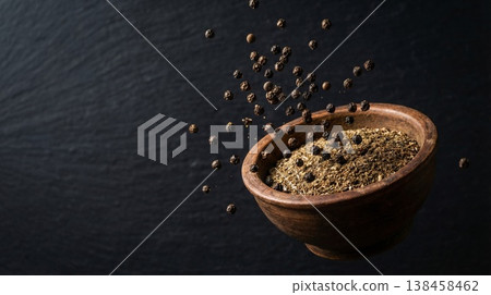 Black pepper falling into wooden bowl with spices on dark background with copy space 138458462