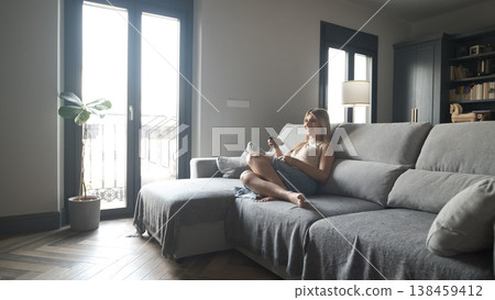 Happy transgender woman using remote control while watching TV at home Happy transgender woman using remote control while watching TV at home 138459412