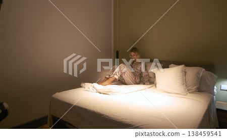 Transgender woman in nightwear sitting with duvet on bed 138459541