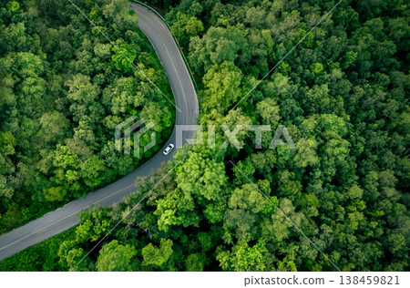 Aerial top view of electric vehicle driving on highway road in green forest. Sustainable transportation, zero emissions, and eco-friendly mobility for reducing carbon footprints. Road infrastructure. Aerial top view of electric vehicle driving on highway road in green forest. Sustainable transportation, zero emissions, and eco-friendly mobility for reducing carbon footprints. Road infrastructure. 138459821