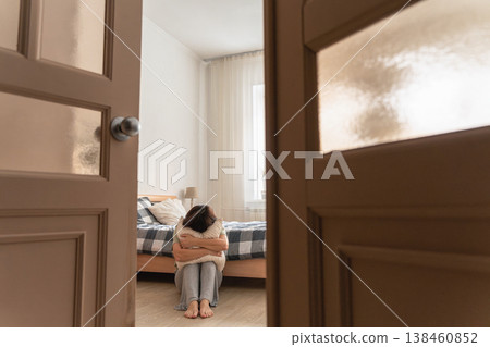 Woman hugging pillow while sitting on bedroom floor, feeling lonely, sad, and suffering from mental health issues Woman hugging pillow while sitting on bedroom floor, feeling lonely, sad, and suffering from mental health issues 138460852