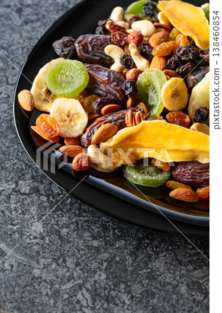 Dried tropical fruits, nuts, and raisins in black plate. Dried tropical fruits, nuts, and raisins in black plate. 138460854
