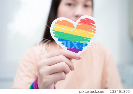 Asian woman holding LGBT heart with rainbow flag. Asian woman holding LGBT heart with rainbow flag. 138461803
