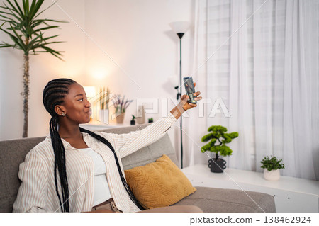 Young Black woman smiling taking selfie with smartphone at home Young Black woman smiling taking selfie with smartphone at home 138462924