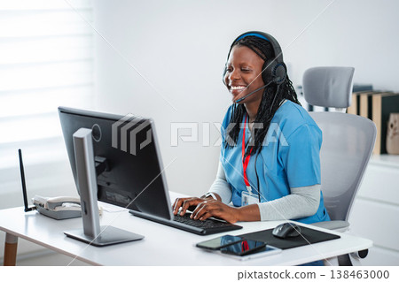 Healthcare professional wearing headset typing on computer Healthcare professional wearing headset typing on computer 138463000