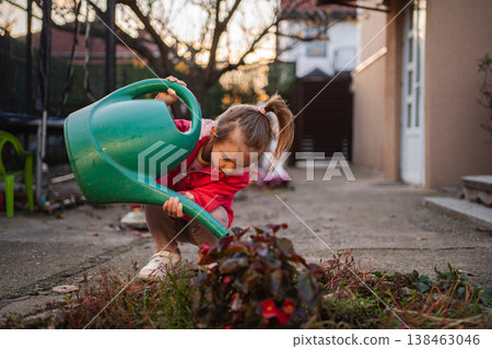 Little girl watering plants with green watering can in yard 138463046