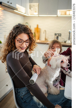 Mother and daughter grooming dog with lint roller in kitchen 138463076