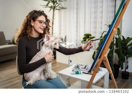 Young adult woman painting on easel with pet dog Young adult woman painting on easel with pet dog 138463102