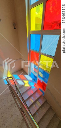 Phone photo of a marble staircase in a shopping center with colorful sunlight streaming through differently colored windows. Vibrant architectural scene showing patterns, light, and modern design. Phone photo of a marble staircase in a shopping center with colorful sunlight streaming through differently colored windows. Vibrant architectural scene showing patterns, light, and modern design. 138463128