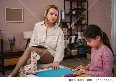 Psychologist observing young girl drawing during child therapy session Psychologist observing young girl drawing during child therapy session 138463580