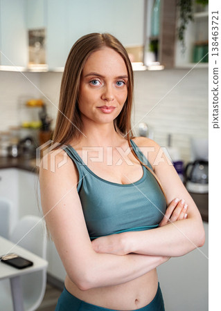 Young adult woman standing with arms crossed in kitchen 138463721