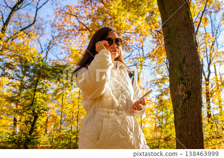 Successful woman in autumn forest talking on smartphone. Mature businesswoman or blogger enjoying nature in park. Concept of lifestyle, freedom, mobile communication and work balance. Successful woman in autumn forest talking on smartphone. Mature businesswoman or blogger enjoying nature in park. Concept of lifestyle, freedom, mobile communication and work balance. 138463999