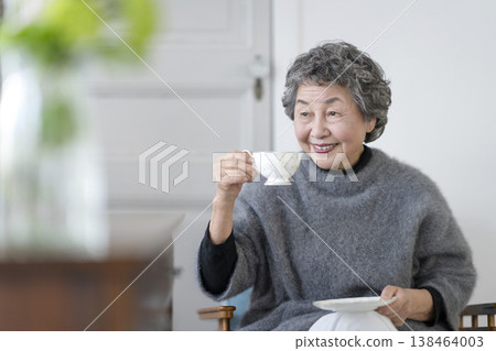 一位微笑的老婦人手捧茶杯。 一位微笑的老婦人手捧茶杯。 138464003