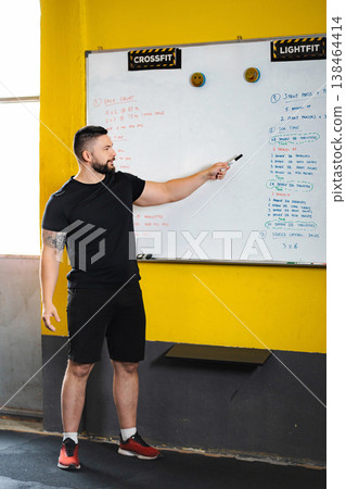 Fitness coach leading CrossFit workout explanation on whiteboard 138464414