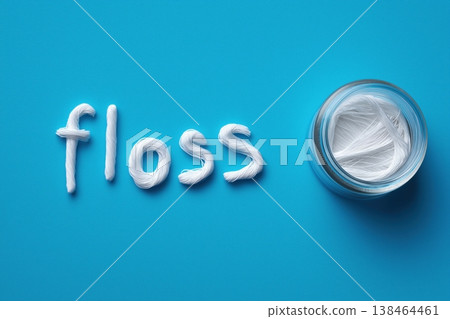 Sparkling white floss spelling 'floss' next to a clean jar of dental thread on blue 138464461