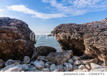 Rocky Coastal Scene With Large Boulders And Calm Sea Under Bright Blue Sky For Nature And Travel Stock Photo 138464753