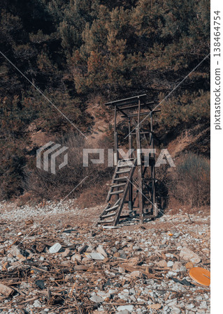 Abandoned Wooden Lookout Tower on Rocky Shore With Debris and Dense Forest Backdrop 138464754