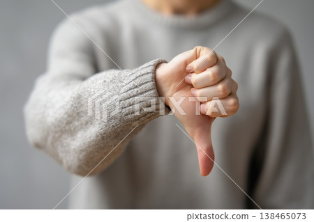Hand gesture showing thumbs down displays disapproval, rejection and failure over gray backdrop with negative emotion. 138465073