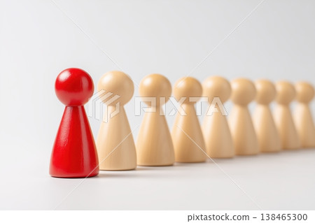 Red game piece stands out among a line of beige wooden figures against a simple background illustrating leadership. Red game piece stands out among a line of beige wooden figures against a simple background illustrating leadership. 138465300