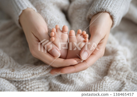 Gentle hands cradle tiny baby feet on a soft knit blanket, symbolizing love, newborn innocence, and tender beginnings. 138465457