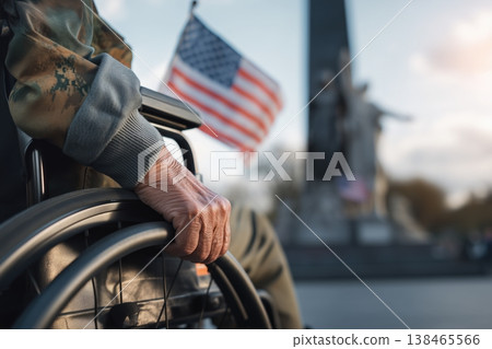 Veteran sits in a wheelchair holding an American flag in honor of service and sacrifice at a memorial site. Veteran sits in a wheelchair holding an American flag in honor of service and sacrifice at a memorial site. 138465566
