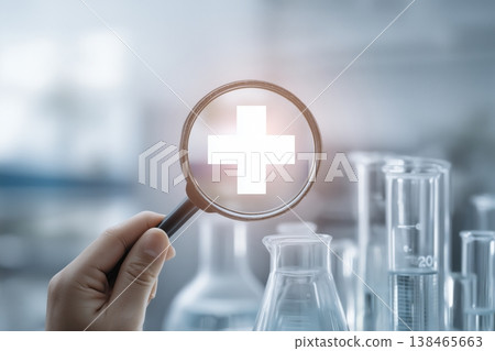 Magnifying glass focuses on a medical cross symbol within a laboratory setting for healthcare advancement. 138465663