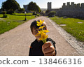 The boy stretches a bouquet of flowers. Focus on hand with flowers. An ancient castle is in the background. Concepts of relationships, gifts, expressions of love, childhood. 138466316