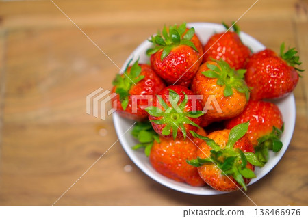 Ripe fresh strawberries in a white bowl on a wooden surface, organic food concept. Ripe fresh strawberries in a white bowl on a wooden surface, organic food concept. 138466976