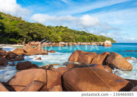 Sunlit tropical beach framed by smooth granite boulders 138466985