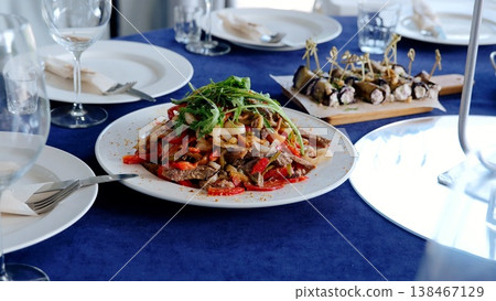 Succulent beef salad with spring greens resting on azure linen, complemented by gleaming silverware and accompanying appetizers Succulent beef salad with spring greens resting on azure linen, complemented by gleaming silverware and accompanying appetizers 138467129