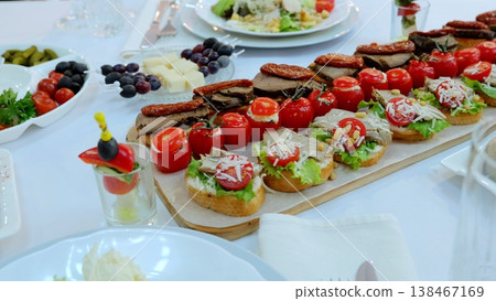 Gourmet appetizer platter featuring miniature sandwiches layered with tomatoes, meat, cheese, lettuce, olives, sundried tomatoes on rustic wooden serving board Gourmet appetizer platter featuring miniature sandwiches layered with tomatoes, meat, cheese, lettuce, olives, sundried tomatoes on rustic wooden serving board 138467169