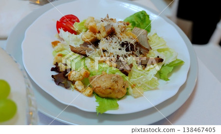 Savory caesar salad combining roasted chicken, crisp croutons, shaved parmesan, pine nuts, and romaine lettuce in vibrant green presentation 138467405