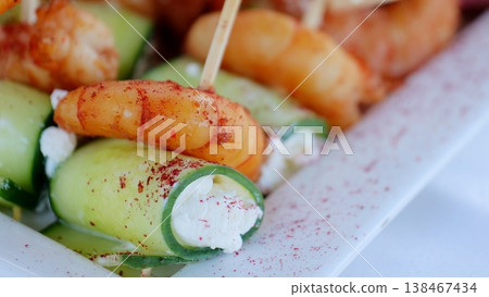 Gourmet appetizer plate displaying cucumber rolls stuffed with creamy filling, garnished with seasoned grilled shrimp, served on crisp white rectangular platter Gourmet appetizer plate displaying cucumber rolls stuffed with creamy filling, garnished with seasoned grilled shrimp, served on crisp white rectangular platter 138467434