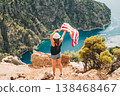 Young woman standing on a rock cliff and waving the US flag while looking at sea beneath. Girl traveller waving the American flag while standing on a mountain top. 4 fourth July Independence Day. 138468467