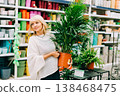 Gardening, planting and shopping concept. Beautiful mature adult woman choosing houseplants and pots in greenhouse or garden centre. Senior buying flowers plants at market store in mall 138468475