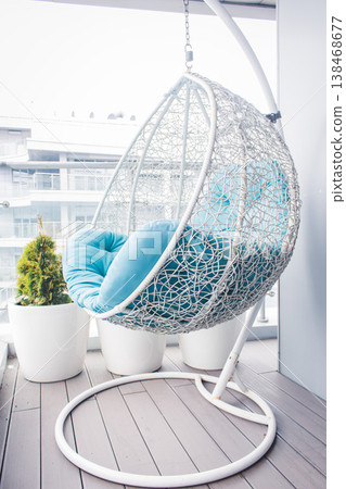 Cozy modern apartment concept. Cozy wicker hammock on balcony. Hanging chair with a blue pillow on wooden terrace. Luxury house design. Dream house decoration. Comfortable home with modern furniture. Cozy modern apartment concept. Cozy wicker hammock on balcony. Hanging chair with a blue pillow on wooden terrace. Luxury house design. Dream house decoration. Comfortable home with modern furniture. 138468677
